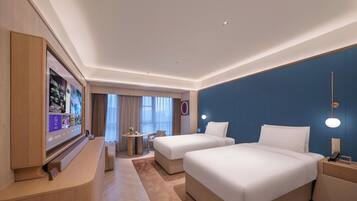 A hotel room with two beds, a desk, a TV, and a view of the outside.