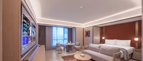Ein modernes Hotelzimmer mit großem Flachbildfernseher, einer Couch, einem Bett, einem Couchtisch und einem kleinen runden Tisch mit Stühlen.