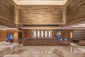 Un lobby moderno con una recepción central, paneles de madera y un quiosco informativo digital.