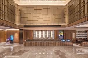 Un lobby moderno con una recepción central, paneles de madera y un quiosco informativo digital.