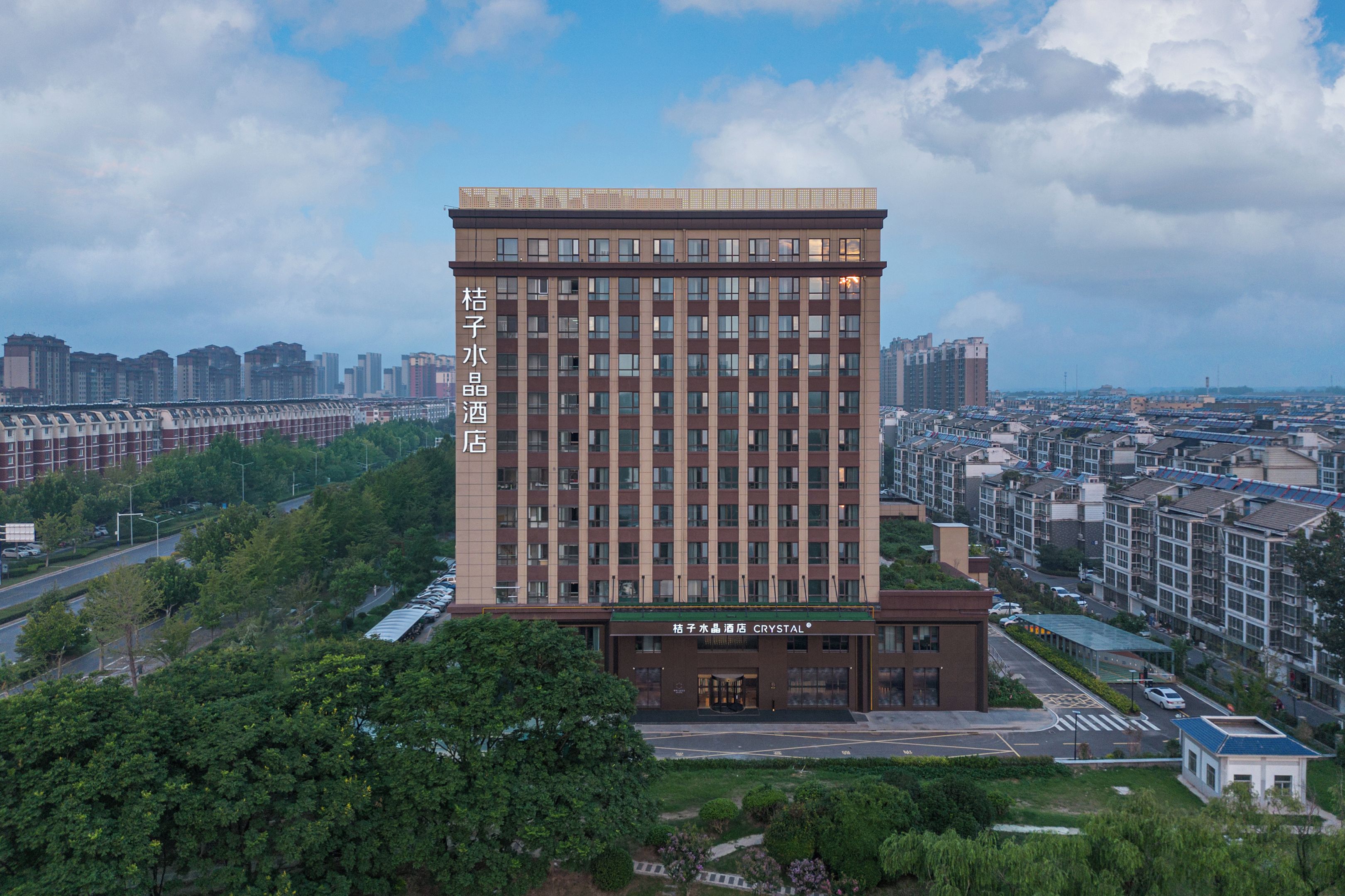 A modern hotel with a prominent name on the facade, surrounded by greenery and other buildings.