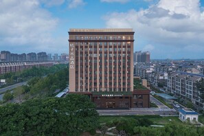 Un hotel moderno con un nombre destacado en la fachada, rodeado de vegetación y otros edificios.