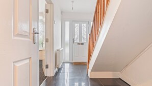 Un couloir avec une porte blanche, un escalier en bois et un radiateur.