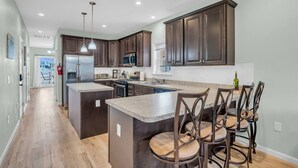 A modern kitchen with dark wood cabinets, a central island with bar stools, stainless steel appliances, and pendant lighting. - Bayview Oasis in the Heart of Seaside Heights (Seaside Heights)