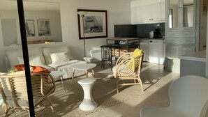Un salon moderne comprenant un canapé, deux petites tables d’appoint blanches, un fauteuil en osier et un coin repas avec une table et des chaises.