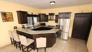 Una cocina con armarios de madera oscura, encimera de granito, refrigerador de acero inoxidable e isla integrada con taburetes de bar.
