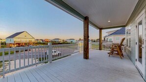 A covered porch with a wooden deck, white railing, and a single wooden chair.