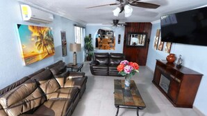 A living room with a sofa, a coffee table with flowers, a TV, and a fireplace. - Stylish Getaway with Private Pool, Fire Pit & Xbox – Walk to the Beach! (Puerto Peñasco)