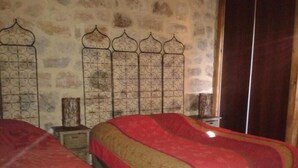 Ein Schlafzimmer mit zwei Betten, beide mit roter und goldener Bettdecke. Der Raum hat eine Steinwand und ein Metall-Kopfteil mit einem Dekor.