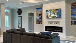Un salon moderne avec un canapé d’angle, un téléviseur à écran plat fixé au mur, une cheminée et un ventilateur de plafond.