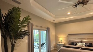 Une chambre à coucher comprenant un lit, un ventilateur de plafond, une table de chevet, une lampe et une porte-fenêtre coulissante donnant sur un espace extérieur.