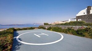A helipad with a 'H' symbol, surrounded by greenery and a building with a stone facade. - Serenity View Villa with Caldera view, heated pool & hot tub in private garden (Thira - Santorini)