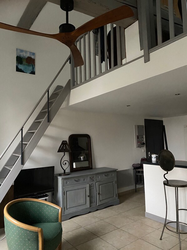 A spacious living area with a staircase leading to an upper floor, a green armchair, a cabinet with a mirror, and a television.
