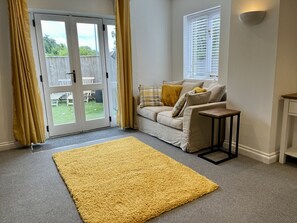 A room with a sofa, a small table, a yellow rug, and a sliding glass door leading to an outdoor area.