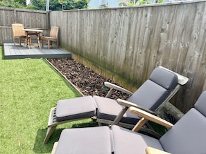 A backyard with a wooden deck, a small table and chairs, and a garden bed with mulch.