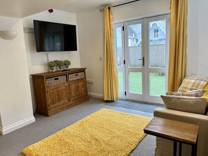 A living room with a flat-screen TV, a wooden cabinet with baskets, a yellow rug, a beige sofa, and a sliding glass door leading to a backyard.