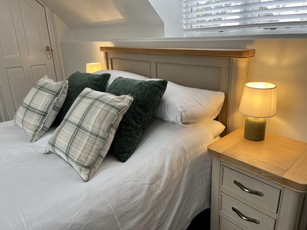 A bed with a headboard, pillows, a bedside lamp, and a nightstand with drawers.