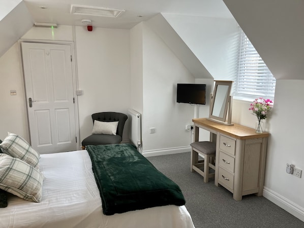 A bedroom with a bed, a chair, a desk, a TV, and a window with blinds. - Detached Cottage with private garden and hot tub. (St Austell)