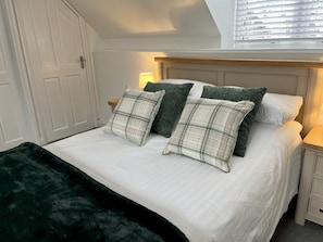 A neatly made bed with white linens and plaid pillows, a dark green throw blanket, and a wooden headboard. - Detached Cottage with private garden and hot tub. (St Austell)
