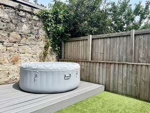 Un bain à remous sur une terrasse en bois, avec un mur en pierre et une clôture en bois en arrière-plan.