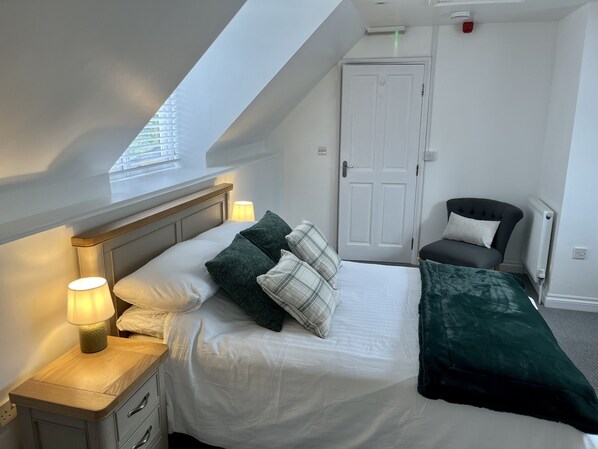 A bedroom with a bed, bedside table, lamp, chair, and a door.
