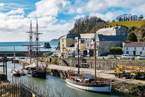 A coastal town with a historic ship docked at the harbor, stone buildings, and a clear view of the sea.