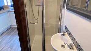 Un bagno moderno con cabina doccia in vetro, un lavabo bianco con specchio sopra e pavimento in legno.