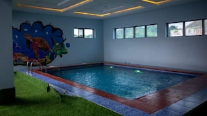 An indoor swimming pool with a mural, windows, and a ceiling with geometric lighting. - Meraki Apartments (Akure)