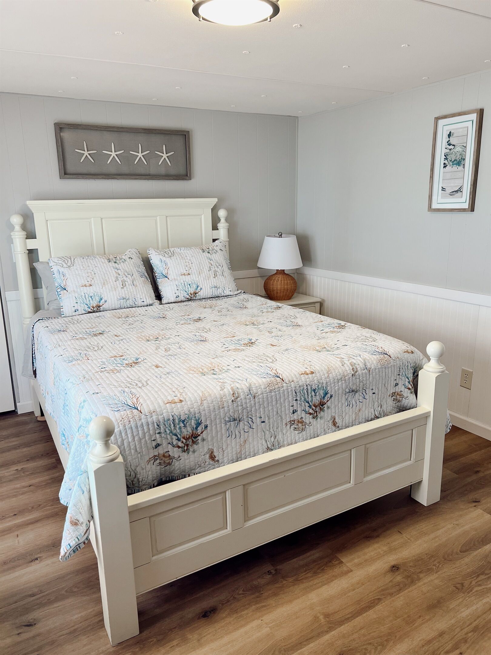 A bedroom with a white bed, floral bedding, a bedside lamp, and a wall decoration.