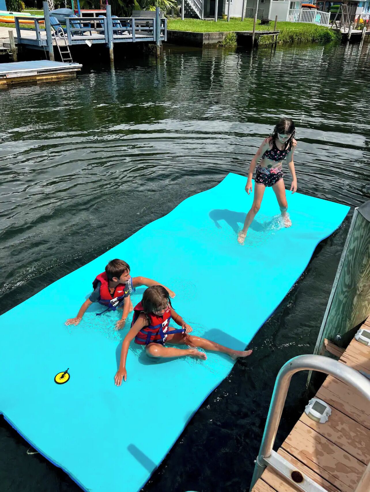 Un espace dédié aux activités nautiques, comprenant une plateforme flottante, un quai et une zone herbeuse, avec un bâtiment visible en arrière-plan.
