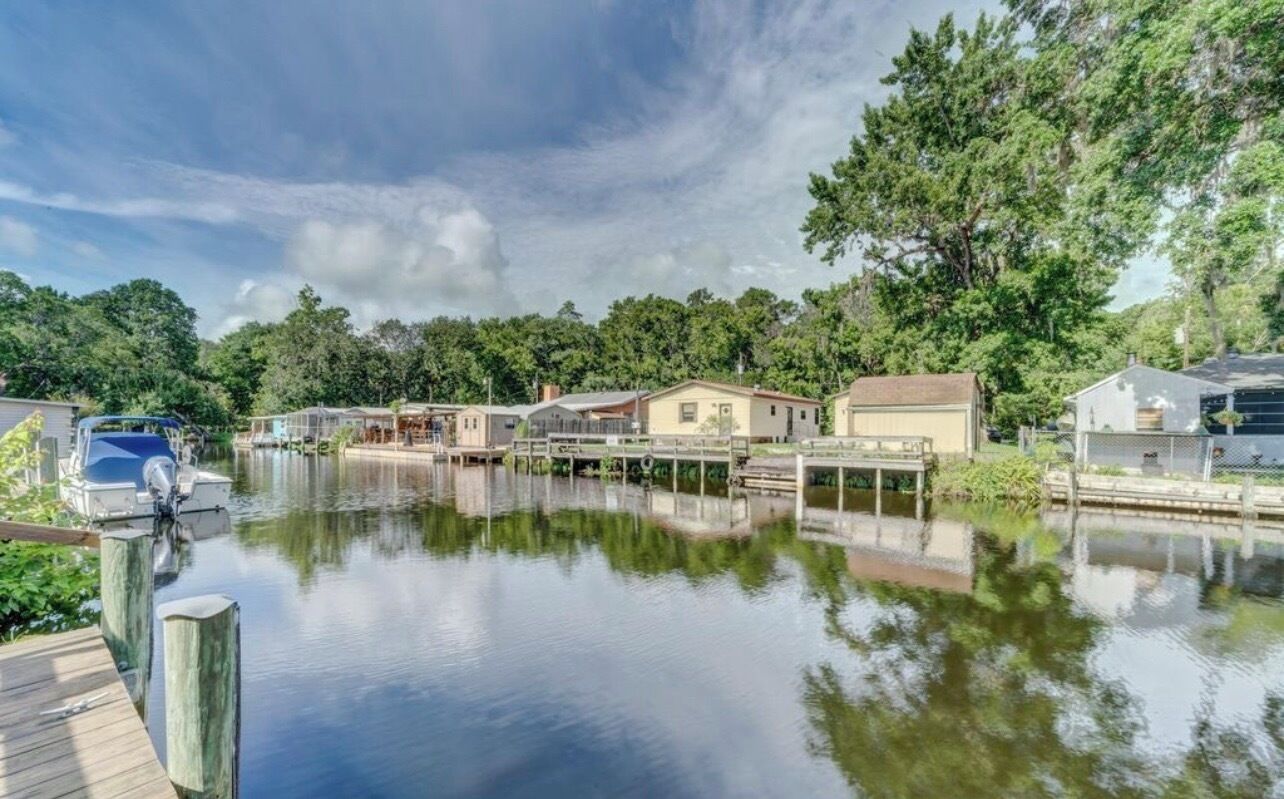 A calm water body with docked boats, a wooden pier, and residential buildings with a dock.