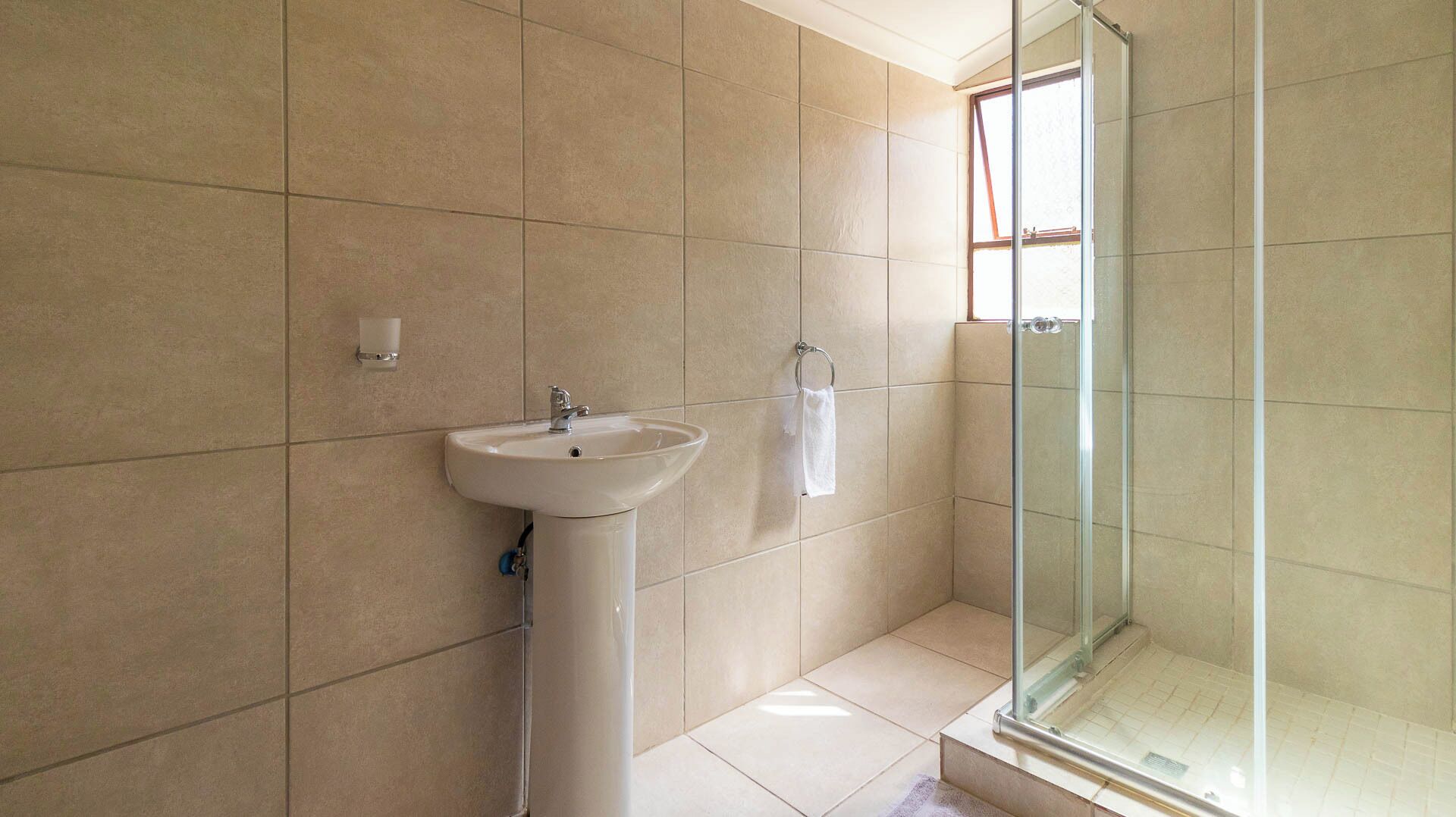 A bathroom with a sink, a glass shower enclosure, and a window.