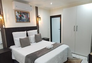 Habitación de hotel con una cama grande, un armario, una mesita de noche, un equipo de aire acondicionado y una obra de arte colgada en la pared.