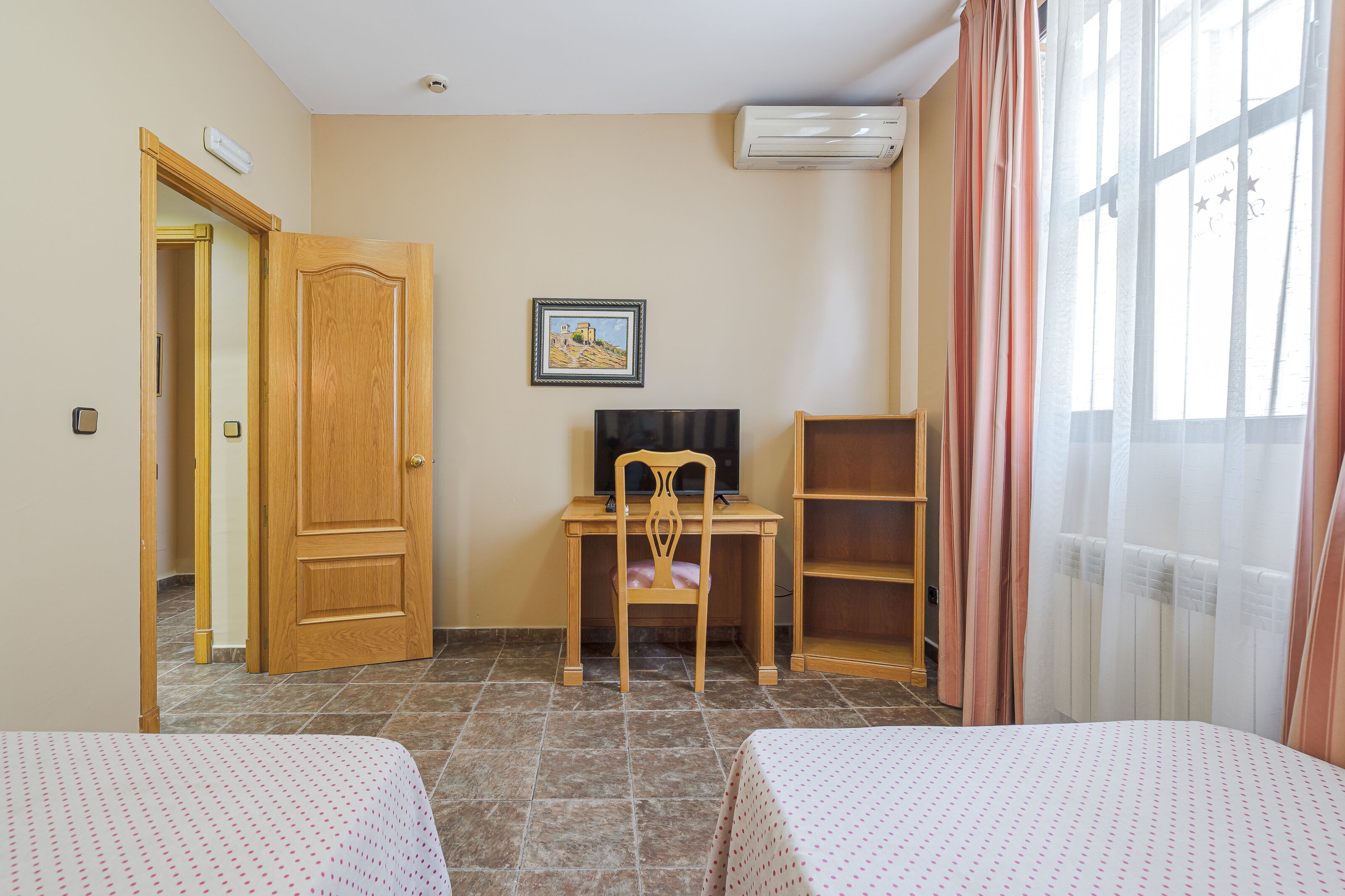 A hotel room with two beds, a desk with a chair, a television, and a picture on the wall.