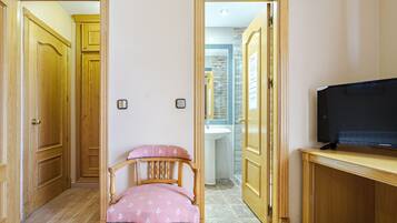 A room with wooden doors, a pink chair, a television on a wooden stand, and a bathroom visible through an open door.