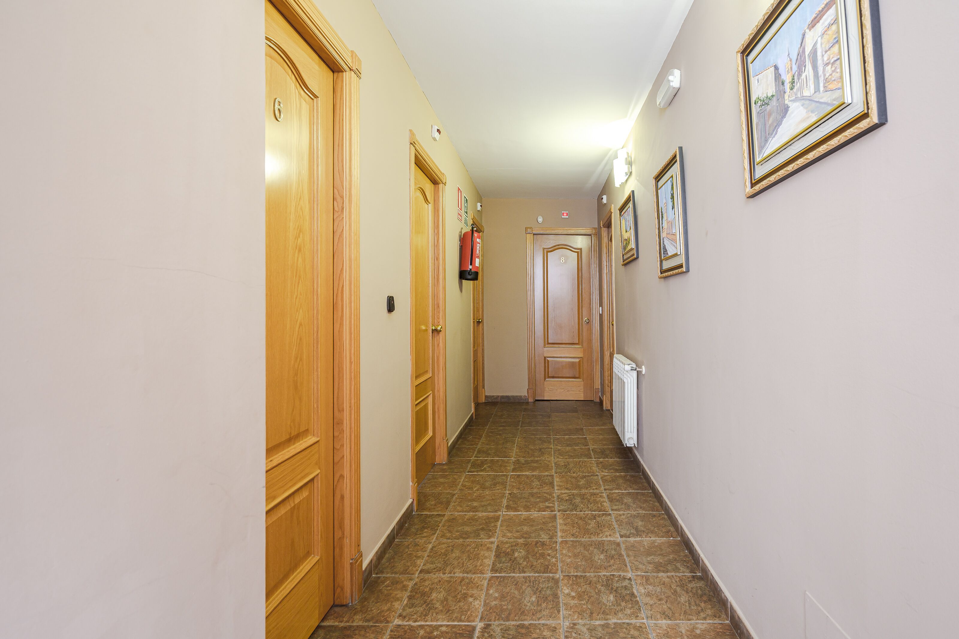 A hallway with wooden doors, a radiator, and framed pictures on the wall.