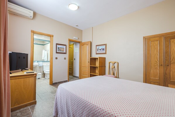 A hotel room with a bed, a television, a wardrobe, and a bathroom visible through an open door. - Hostal Don Juan (Meco)