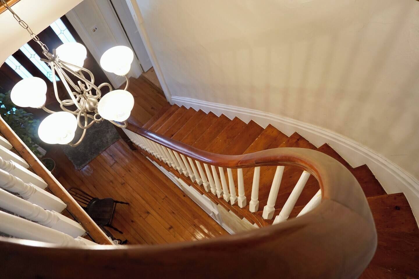 Un escalier en colimaçon avec des marches en bois et des balustrades blanches, menant à un palier agrémenté d’un lustre.