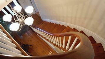 Un escalier en colimaçon avec des marches en bois et des balustrades blanches, menant à un palier agrémenté d’un lustre.