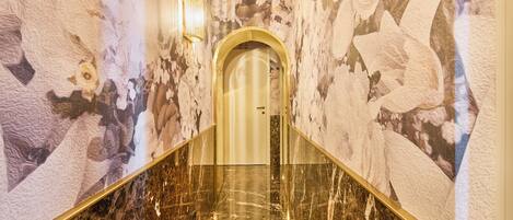 A marble staircase with a golden handrail leading to a door with a floral mural on the walls.