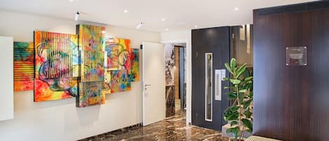 Un vestíbulo moderno con suelo de mármol, arte abstracto de colores, un banco de madera y una planta en maceta.