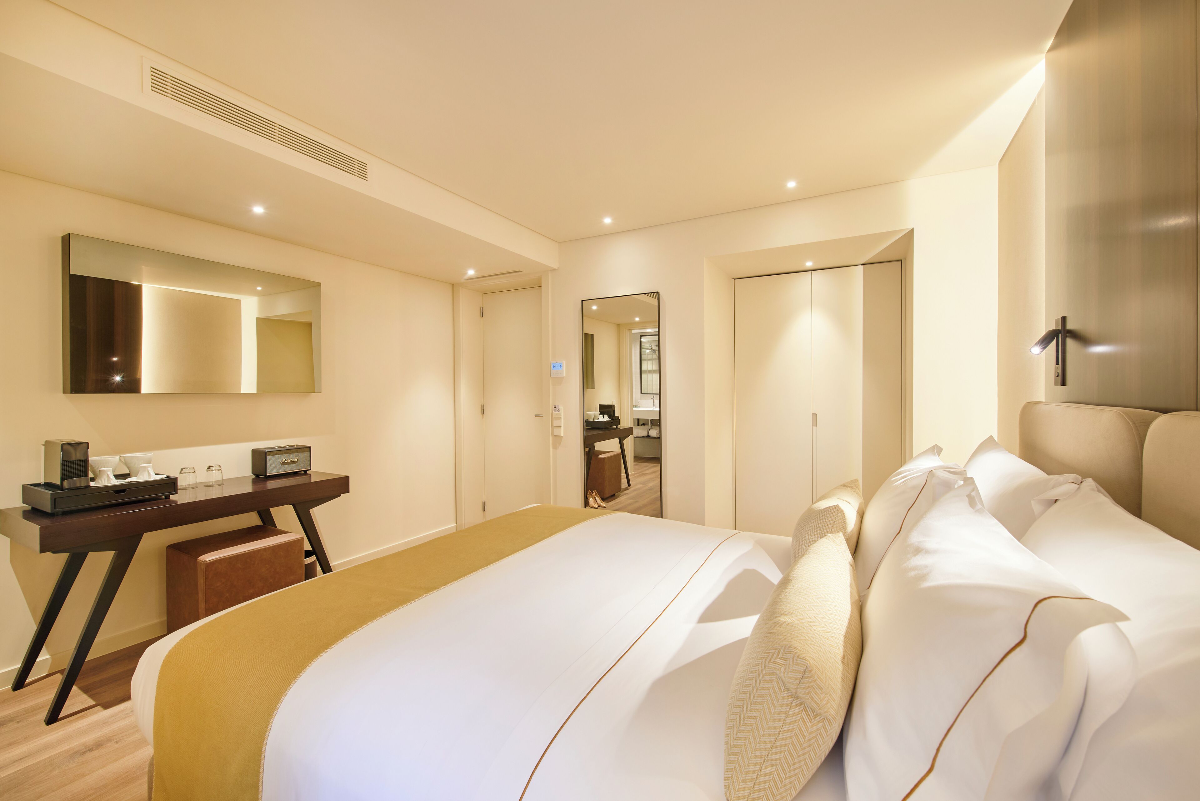 Una habitación de hotel con una cama grande, un escritorio con una silla, un espejo y un armario.