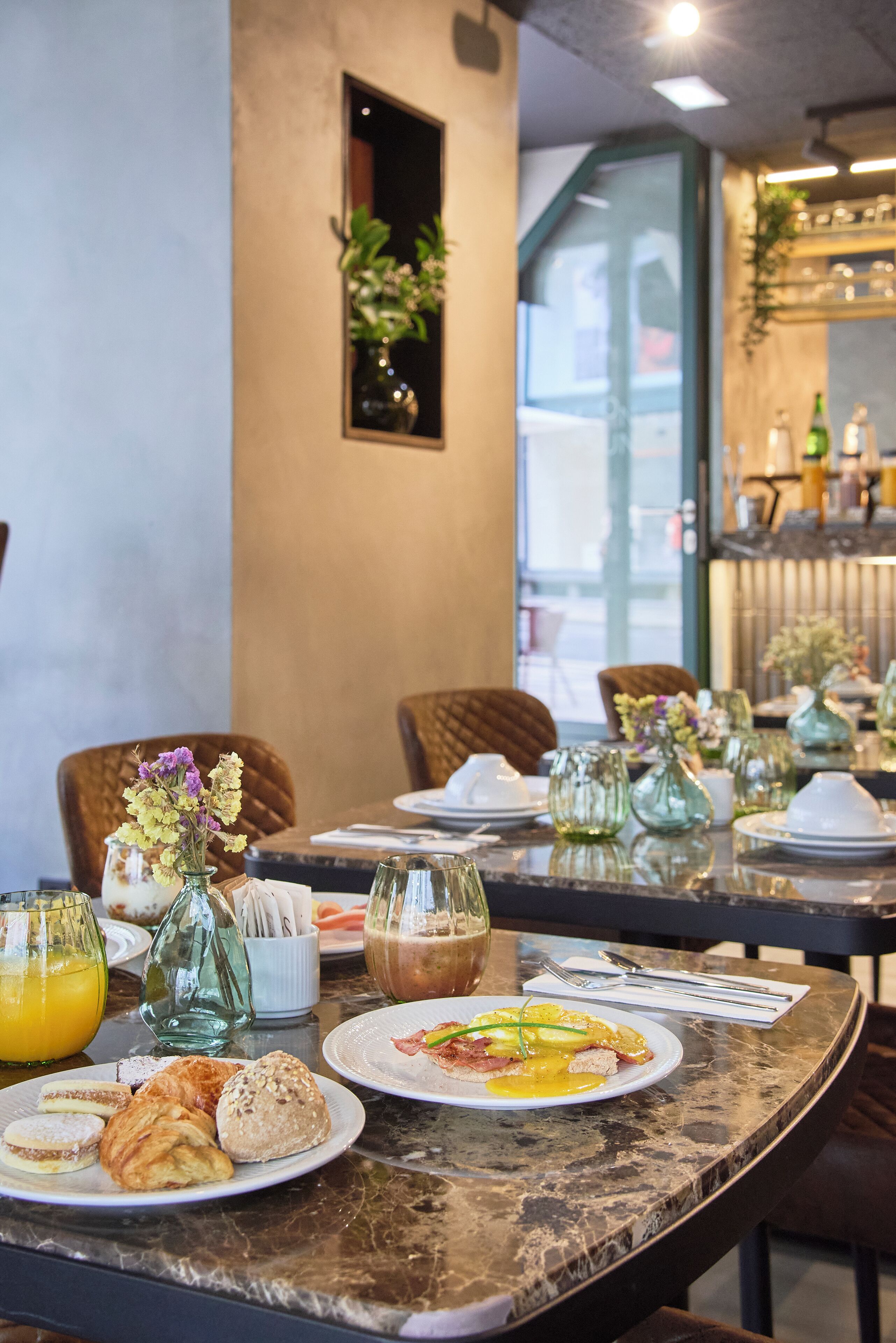 A breakfast setting with a marble table, various dishes, and a vase with flowers.