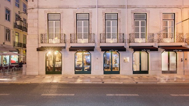 Un hotel de varios pisos con un estilo arquitectónico europeo clásico, con balcones y tiendas en la planta baja.