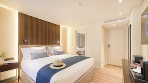 Una habitación de hotel moderna con una cama grande, una mesita de noche con lámpara, un espejo y un escritorio con computadora.