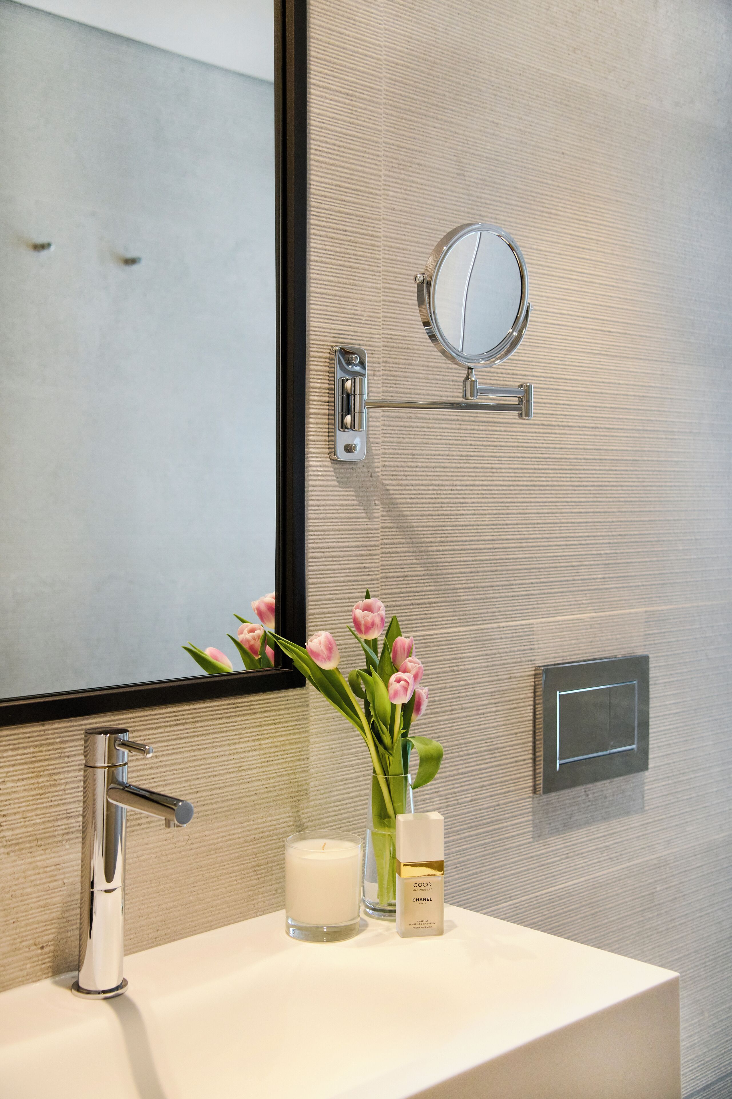 Un tocador de baño con espejo, lavabo, vela y un florero con flores.