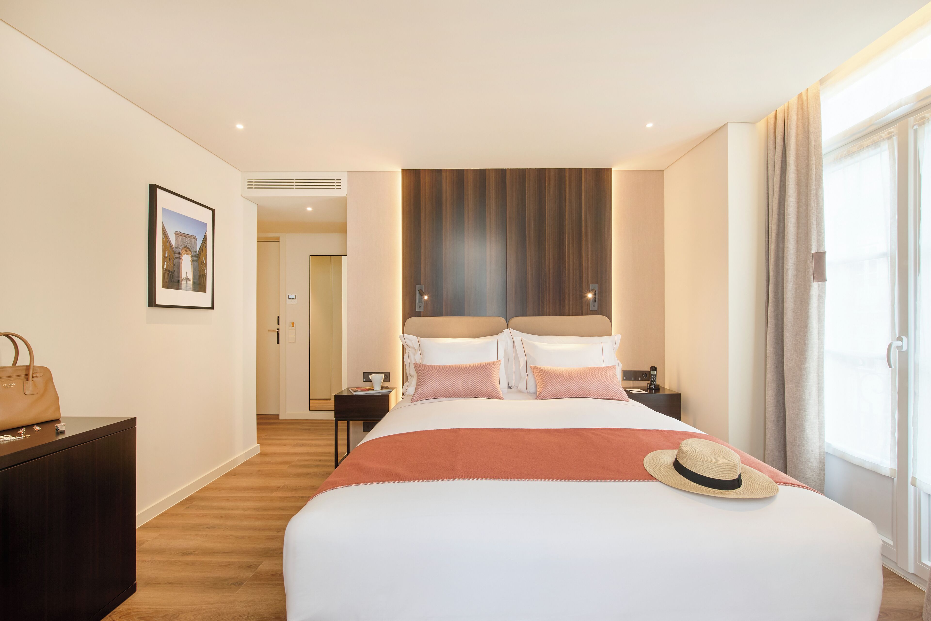 Ein Hotelzimmer mit einem großen Bett, einem Nachttisch, einer Kommode und einem Fenster mit Vorhängen.