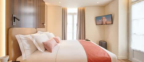 A hotel room with a large bed, a flat-screen TV mounted on the wall, a window with curtains, and a wall-mounted light fixture.