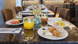 Un desayuno con una variedad de platos, incluyendo frutas, pasteles y bebidas, dispuesto sobre una mesa de mármol en un restaurante.
