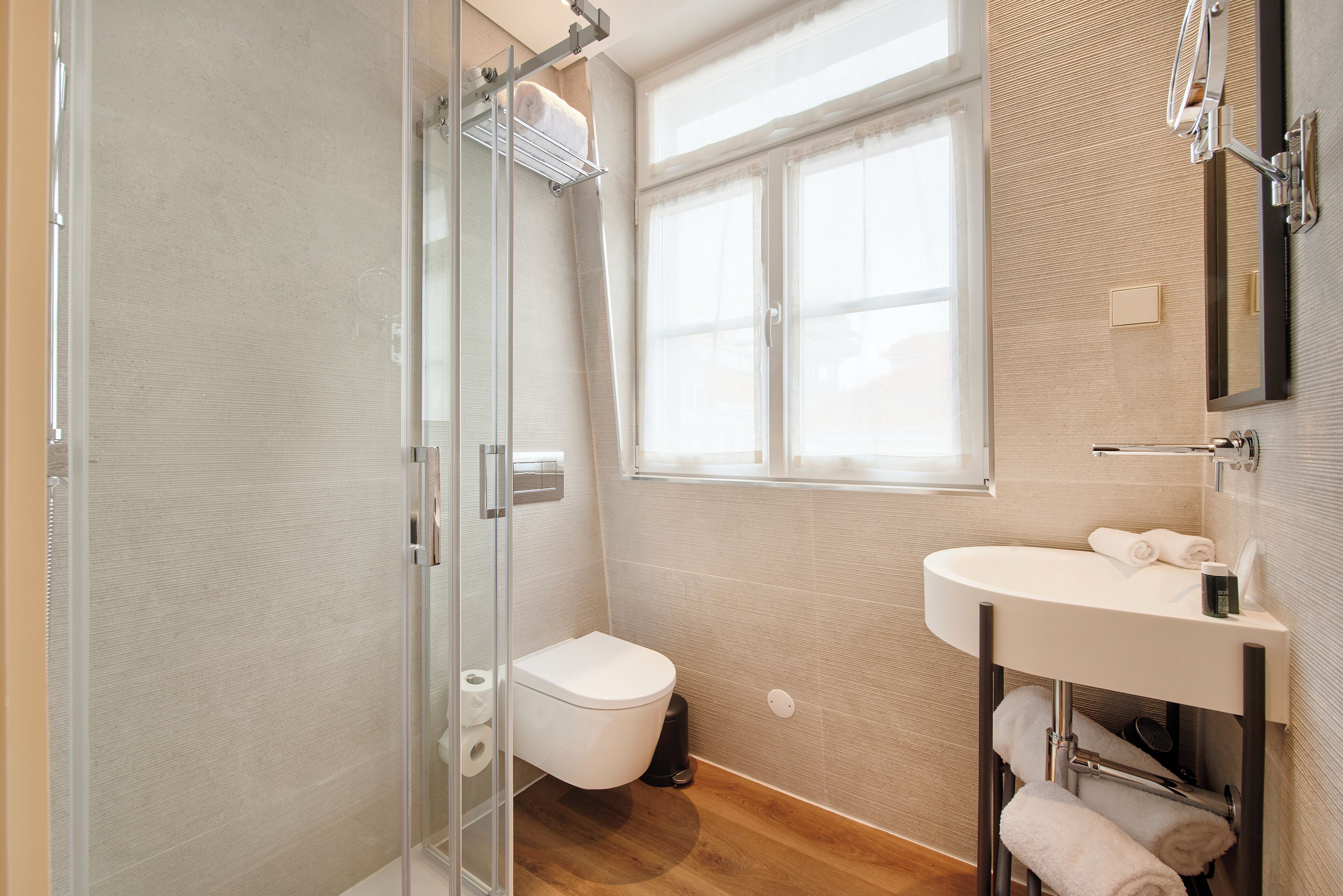 A modern bathroom with a glass shower enclosure, a white toilet, a sink with a mirror, and a window providing natural light.